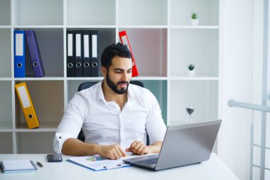 Masada oturan ve dizüstü bilgisayar kullanma office genç yakışıklı girişimci.