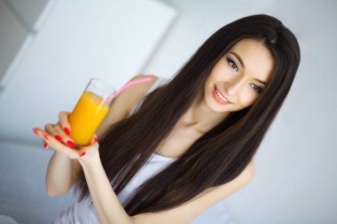 Neşeli kadın evde yatağında portakal suyu içiyor.