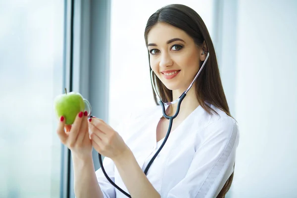 Health. Healthy Diet. Doctor Dietitian Holding in Hands Fresh Green Apple and Smiles. Beautiful and Young Doctor. High Resolution