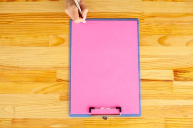 Office el a ağıl ile pembe renk kağıt ve kalem ahşap masa arka plan üzerinde tutarak. Boşaltmak. Metin için yer.