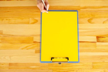 Bir klasörü bir sarı renk kağıt ve kalem ahşap masa arka plan üzerinde tutan office el. Boşaltmak. Metin için yer.