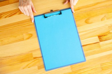 Bir klasörü bir mavi renk kağıt ahşap masa arka plan üzerinde tutan office el. Boşaltmak. Metin için yer.