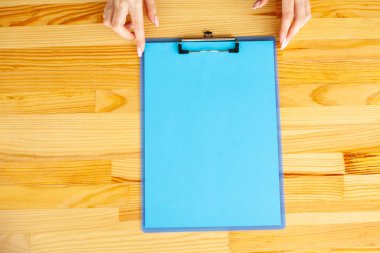 Bir klasörü bir mavi renk kağıt ahşap masa arka plan üzerinde tutan office el. Boşaltmak. Metin için yer.