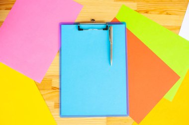 Bir klasörü bir mavi renk kağıt ve kalem ahşap masa renkli arka plan üzerinde tutan office el. Boşaltmak. Metin için yer.