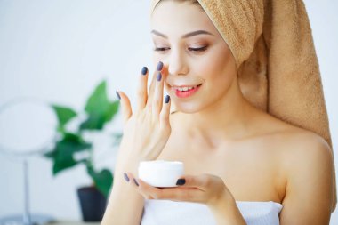 Beauty and Care. Woman with Pure Skin and Towel on the Head Pour Cream on Face. Body Care. Skin Care. High Resolution clipart