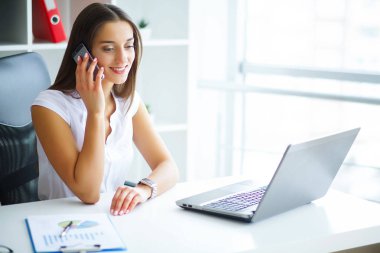 İş. İş kadını Office ve inşaat Computeer ile masada oturur. Kız telefonla konuşuyor. Beyaz bluz giymiş kadın. Yüksek çözünürlük