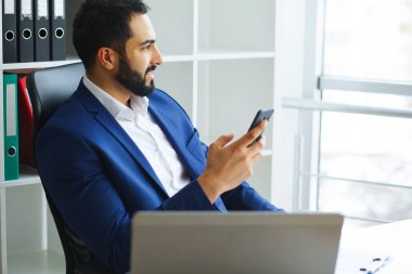 İş. Işık ve tutan eller telefonda mutlu iş adam oturur. Gülümseyen genç adam ve bilgisayar tarafından çalışır. Yüksek çözünürlük