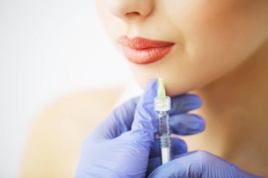 Kadın dudaklarına botoks yapan kozmetik uzmanının ellerine yakın çekim. Elinde şırınga var. Genç ve güzel bayan keyifle prosedür uygulanıyor.