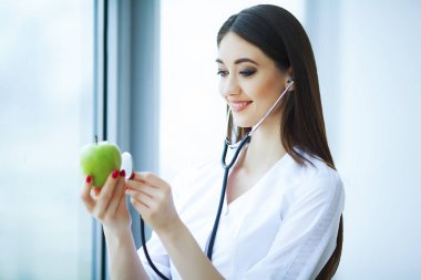 Sağlık ve güzellik. Doktor diyetisyen pencerenin önünde ışık Office yakınındaki ayakta. Kızı tutan Apple el ve gülümsüyor. Doktor gösterir Apple