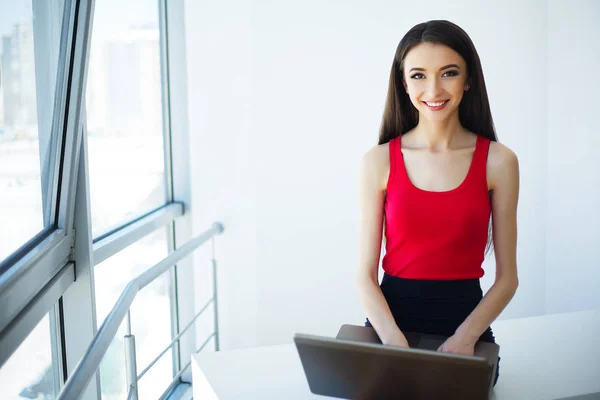 穿着红色 T恤衫和黑色短裙的商业妇女正在电脑上工作 女孩坐在桌子上 微笑着 高分辨率 — 图库照片