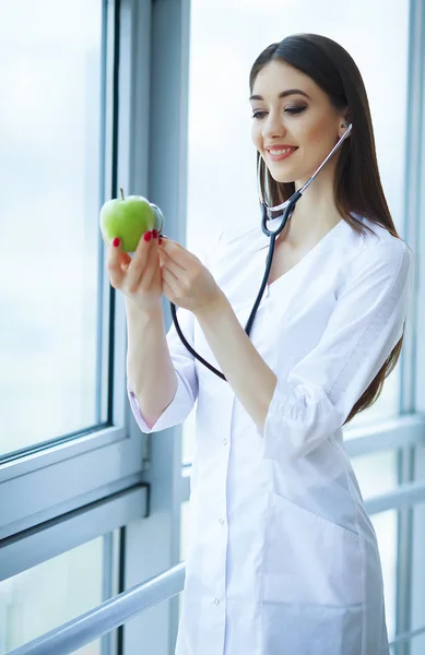 Health and Beauty. Doctor Dietitian Standing near the Window at the Light Office. Girl Holds Apple in Hands And Smiles. Doctor Shows Apple