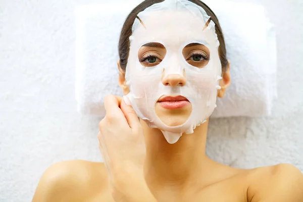 Kozmetik maskesi yüzünde güzel bir kadın. Kız beyaz bir arka plana dayanır Spa salonda tedavi alır. Ev yapımı maske yüz için. Spa uygulamaları.