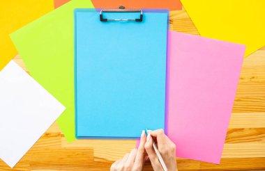 Bir klasörü bir mavi renk kağıt ve kalem ahşap masa renkli arka plan üzerinde tutan office el. Boşaltmak. Metin için yer.