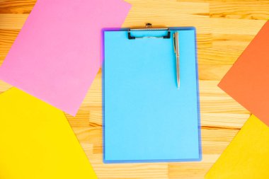 Bir klasörü bir mavi renk kağıt ve kalem ahşap masa renkli arka plan üzerinde tutan office el. Boşaltmak. Metin için yer.