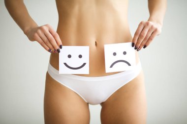 Kadın sağlık sorunu. Kadın üzgün gülen yüz midesini yakınındaki beyaz kartı tutan külot içinde uygun ince gövdeli closeup. Sindirim bozuklukları, adet ağrısı, sağlık sorunları kavramı.