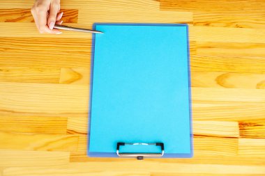 Bir klasörü bir mavi renk kağıt ahşap masa arka plan üzerinde tutan office el. Boşaltmak. Metin için yer.