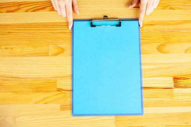 Bir klasörü bir mavi renk kağıt ahşap masa arka plan üzerinde tutan office el. Boşaltmak. Metin için yer.