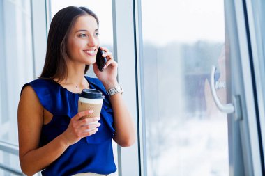 İş. Mavi tişört ve siyah etek giymiş bir genç kadının portresi. Işık Modern ofis büyük penceresinde, ayakta ve gülümseyerek. Yüksek çözünürlük.