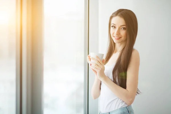 Young pretty business woman with cup of coffee in the bright modern office indoors