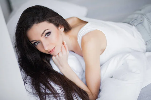 白いベッドでくつろいで笑顔かなり若いブルネットの女性の肖像画 — ストック写真