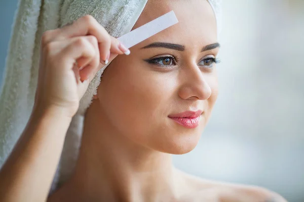 Beautician waxing young woman's eyebrows in spa center.