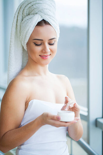 Skin care. Studio shot of beautiful young woman applying moisturizer cream onto her face.