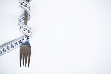 Beslenme veya kilo kontrolü kavramı. Santimetre teyp ve metin eklemek için bir yer ile beyaz bir arka plan üzerinde çatalı. Sağlık, kilo kaybı, diyet, doğru beslenme kavramı.