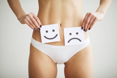 Kadın sağlık sorunu. Kadın üzgün gülen yüz midesini yakınındaki beyaz kartı tutan külot içinde uygun ince gövdeli closeup. Sindirim bozuklukları, adet ağrısı, sağlık sorunları kavramı.