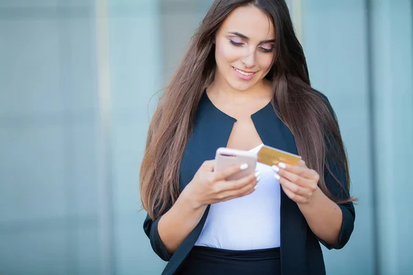 Low Angle Of Pleased Girl Standing at the Airport Hall. He is Using Gold Credit card and Cellphone For Paying.