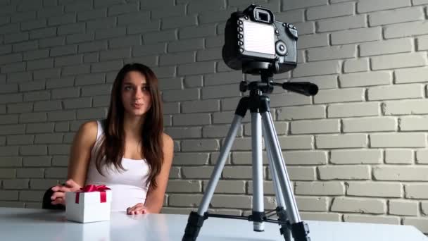 圣诞礼物在录制关于新年礼物的视频博客时, 长头发的年轻女子坐在办公桌前与镜头交谈 — 图库视频影像