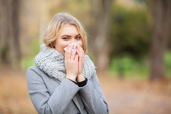 Seorang gadis bersin di tisu. Wanita muda meniup hidungnya di taman. Perempuan potret bersin di luar ruangan karena dingin dan flu — Stok Foto