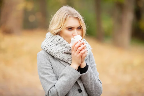 Chica estornudando en tejido. Una joven sonándose la nariz en el parque. Mujer retrato al aire libre estornudos porque el frío y la gripe — Foto de Stock