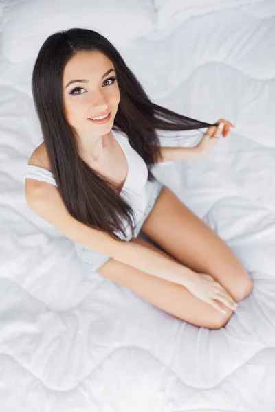 Goedemorgen. Portret van een lachende ontspannen in witte bed mooie jonge brunette vrouw — Stockfoto