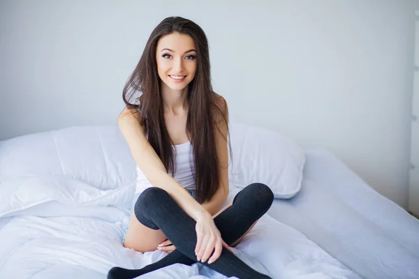 Dobré ráno. Portrét usmívající se hezká mladá brunetka žena v bílé posteli — Stock fotografie