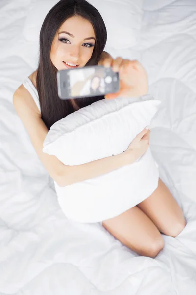 Good morning. Young happy woman taking selfie with mobile phone in bedroom morning
