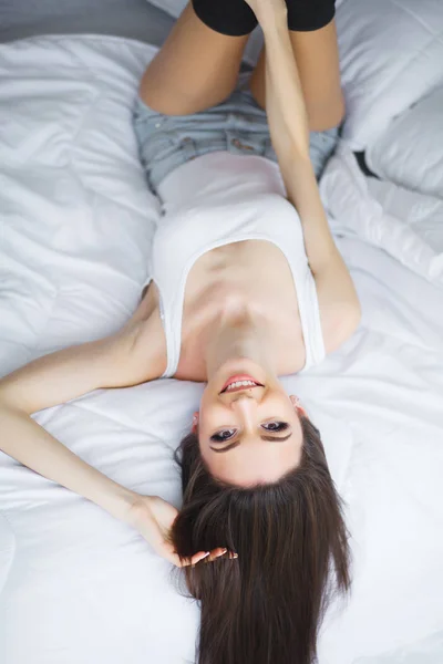 Günaydın. Bir gülümseyen genç ve güzel esmer kadın beyaz yatakta rahatlatıcı portresi — Stok fotoğraf
