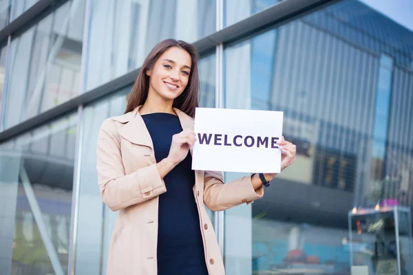 Empresaria con el pelo largo Sosteniendo un cartel Junta con una bienvenida tiene antecedentes Aeropuerto —  Fotos de Stock