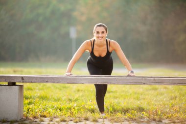 Yan görünümü motive bir Asyalı. Güzel sportif 20'li kadında şınav ve bluetooth kulaklık ile müzik egzersiz sırasında yeşil park dinlemek spor giyim portresi