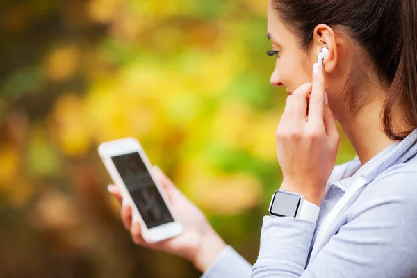 Foto av Joyful Fitness kvinna 30s i sportkläder röra Bluetooth Earpod och hålla mobiltelefon, medan du vilar i Green Park — Stockfoto