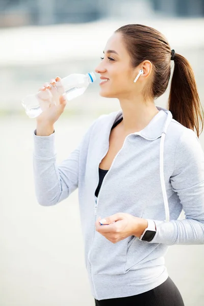 Спорт на открытом воздухе. Спортивная женщина в наушниках пьет воду — стоковое фото