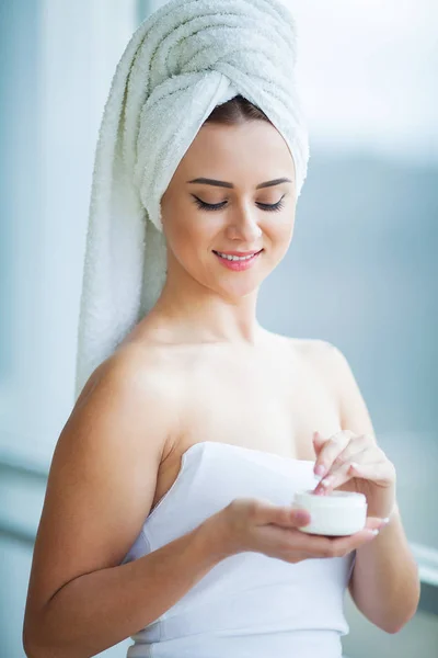 Una mujer hermosa usando un producto para el cuidado de la piel, crema hidratante o loción y cuidado de la piel cuidando su tez seca. Crema hidratante en manos femeninas — Foto de Stock