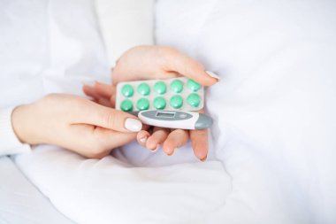 Soğuk algınlığı ve grip. Kadın termometr tutun ve hapları elinde, yatakta yatıyordu blister