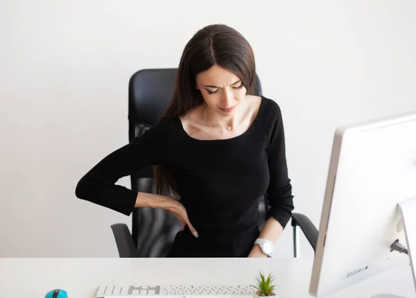 Back pain. Businesswoman sit in her office and feels pain in back