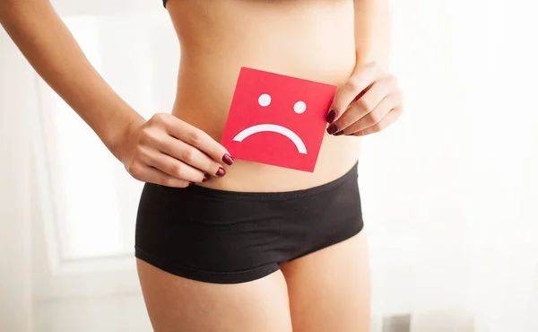 Vaginal or urinary infection and problems concept. Young woman holds paper with sad smile above crotch