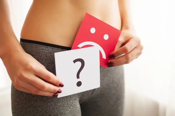 Woman Health Problem. Closeup Of Female With Fit Slim Body Holding Cards With Sad Smiley Face and Question Mark Near Her Stomach. Digestive Disorders, Period Pain, Health Issues Concept