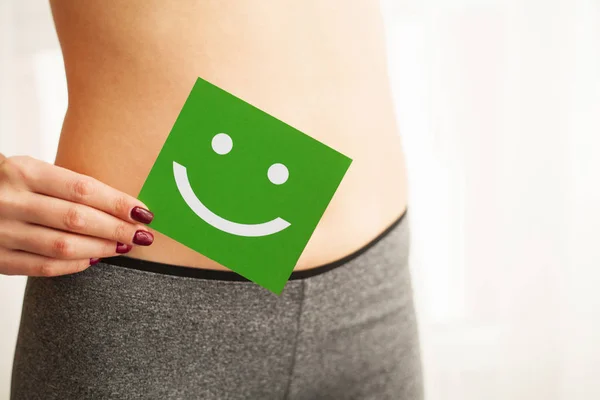 Women Health. Closeup Of Healthy Female With Beautiful Fit Slim Body In Black Panties Holding Green Card With Happy Smiley Face In Hands. Stomach Health And Good Digestion Concepts. High Resolution