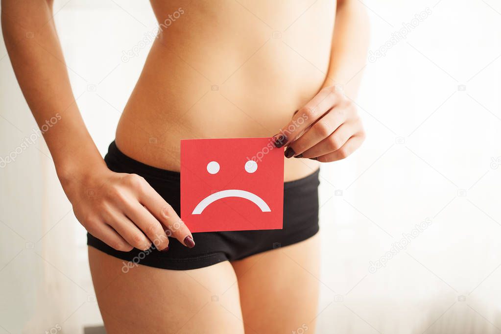 Vaginal or urinary infection and problems concept. Young woman holds paper with sad smile above crotch