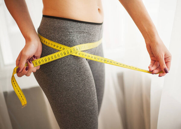 Hands measuring waist with a tape. Slim and healthy woman at her home