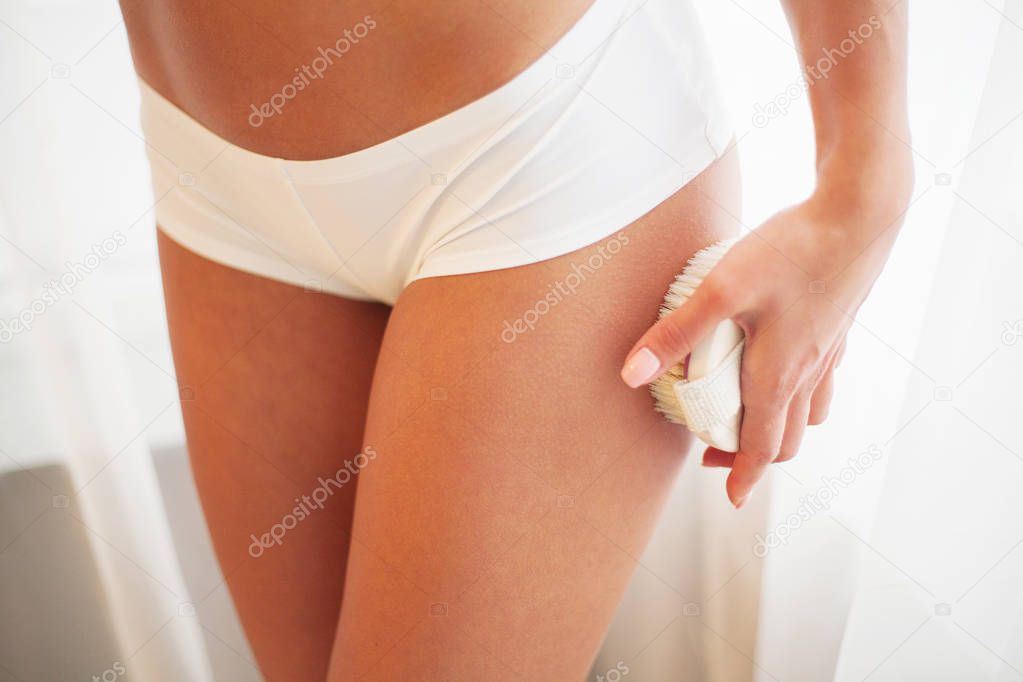 Womans arm holding dry brush to top of her leg. Cellulite treatment, dry brushing