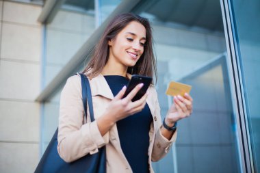 Memnun kız Havaalanı Salonu'nda ayakta düşük açılı. O kullanarak Gold kredi kartı ve cep telefonu için ödeme.